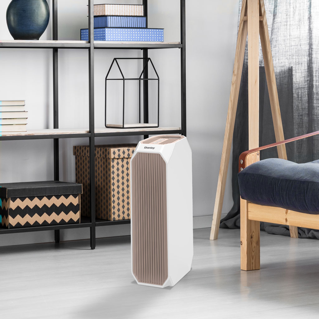 Danby appliances air purifier 210 sq ft DAP143BAW-UV in a home interior setting beside shelving and a chair on a light floor