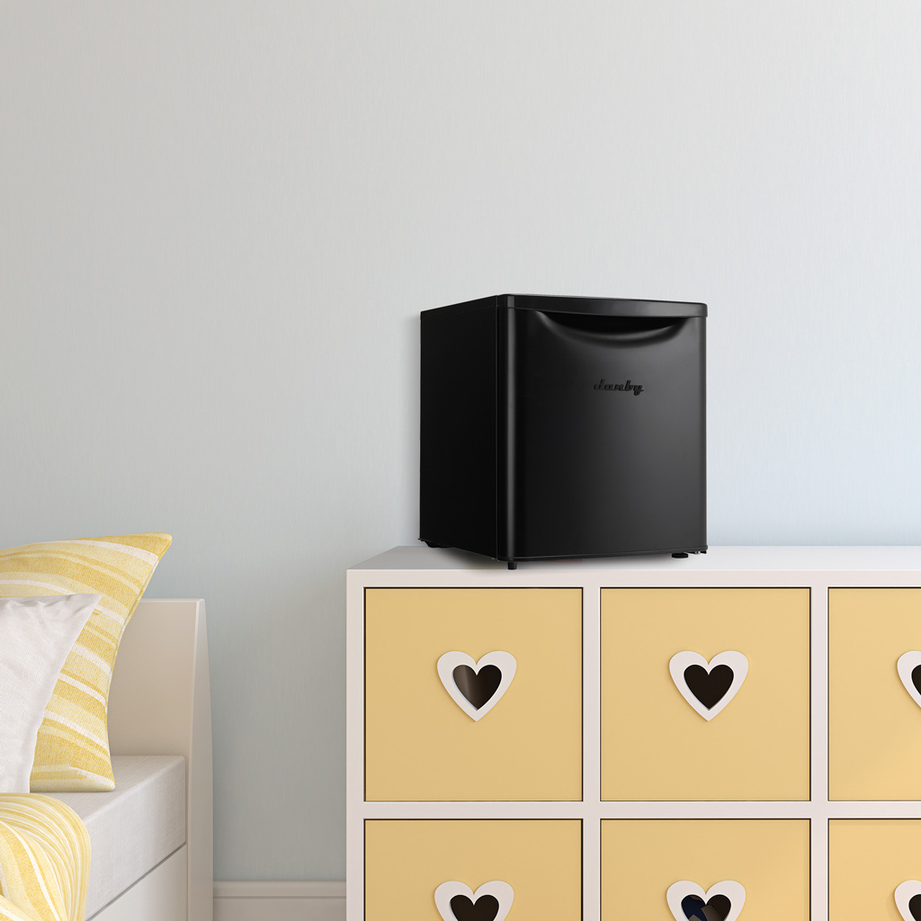 Danby appliances 1.7 cu ft compact fridge black DAR017A3BDB shown on a dresser in a bedroom setting beside a bed and drawers, highlighting compact placement