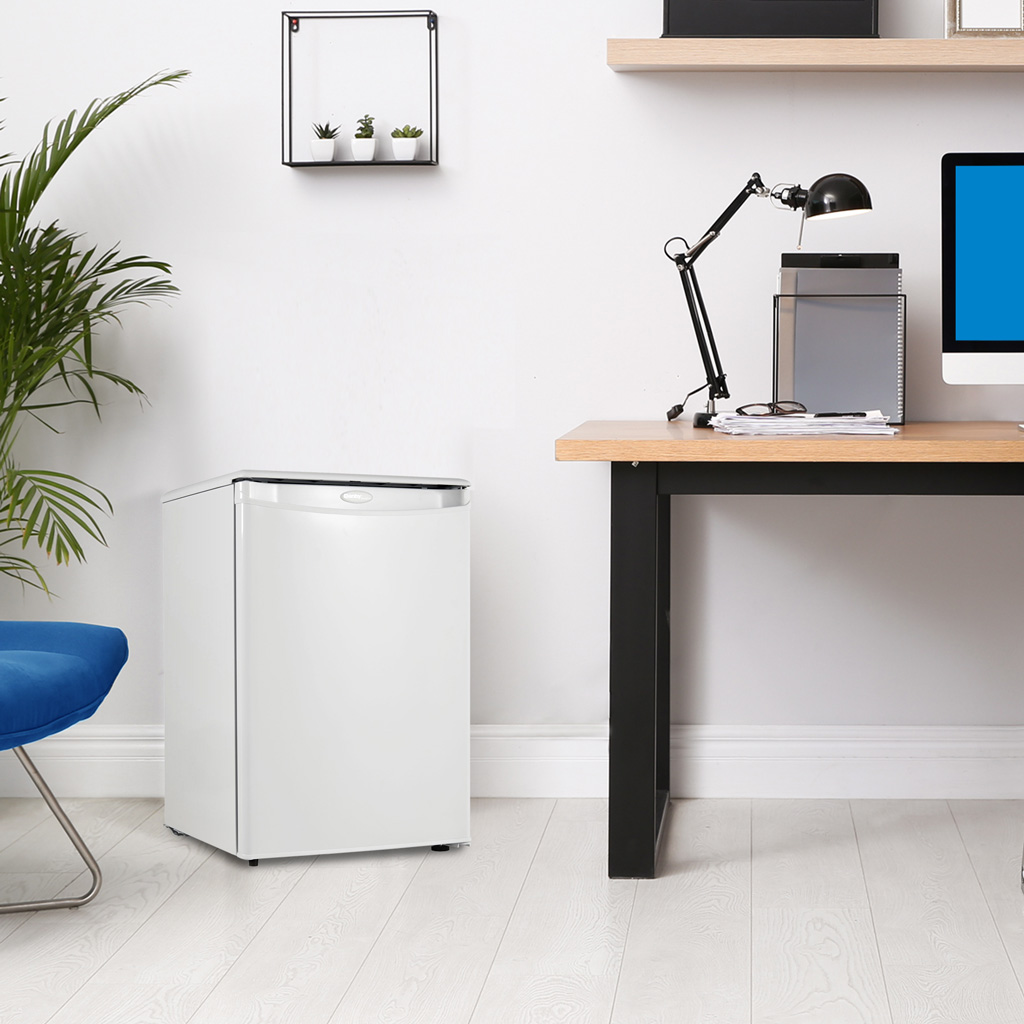 Danby appliances 1.6 cu ft compact fridge white DAR016A1WDD shown beside a desk in a home office setting with chair, lamp, and computer, highlighting compact placement and everyday use