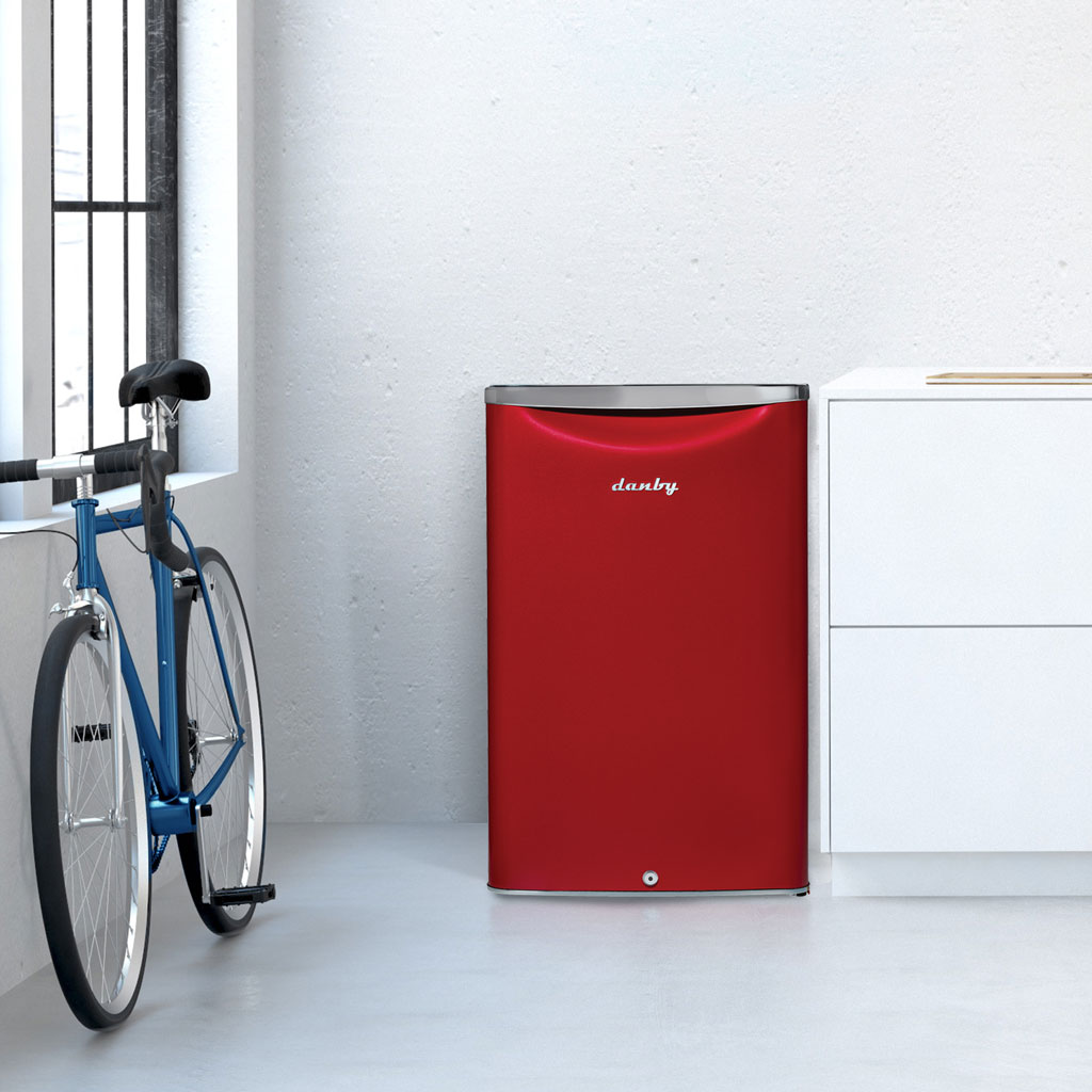 Danby appliances 4.4 cu ft compact fridge red DAR044A6LDB shown in a modern room beside a bicycle and cabinetry highlighting compact placement and contemporary design