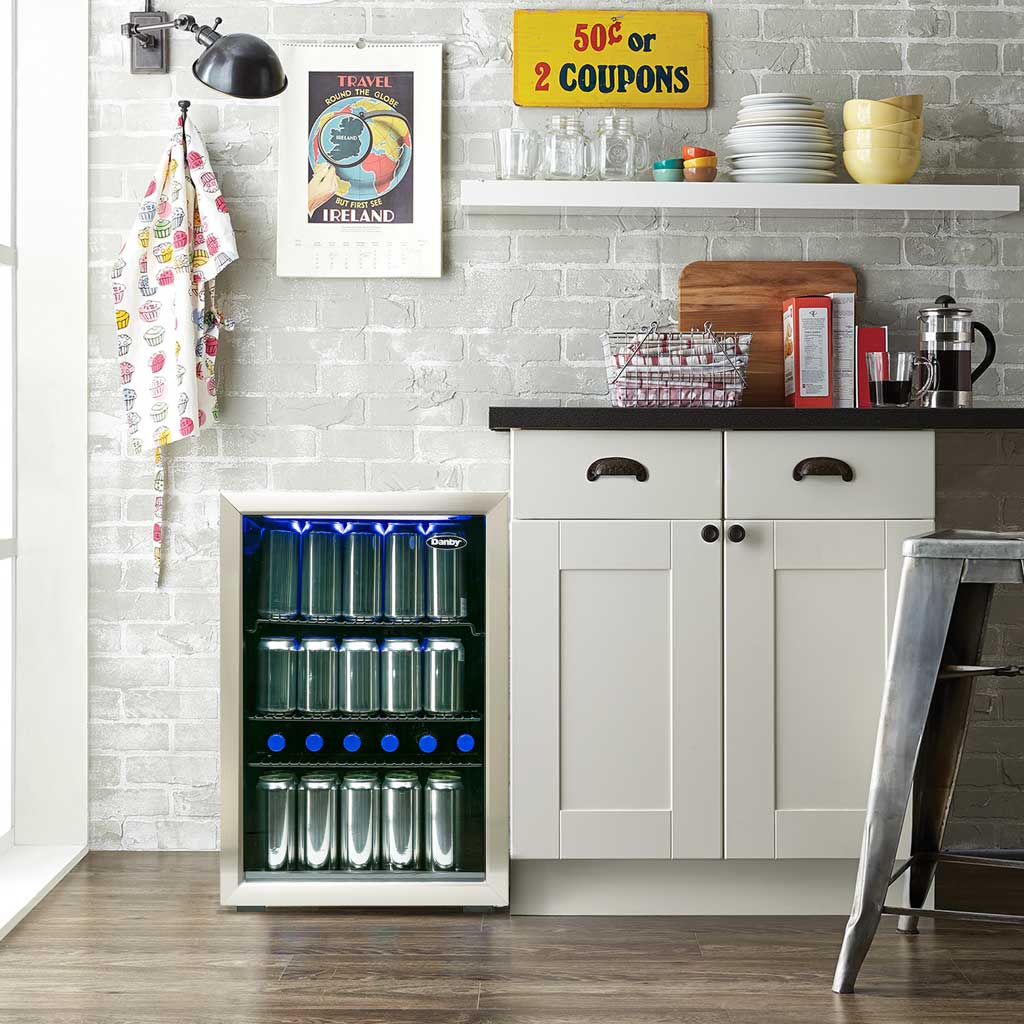 Danby 2.6 cu. ft. Free-Standing Beverage Center in Stainless Steel 6 Danby appliances 2.6 cu ft beverage center stainless DBC026A1BSSDB shown in a kitchen setting beneath a countertop beside cabinetry, displaying interior shelves stocked with beverage cans