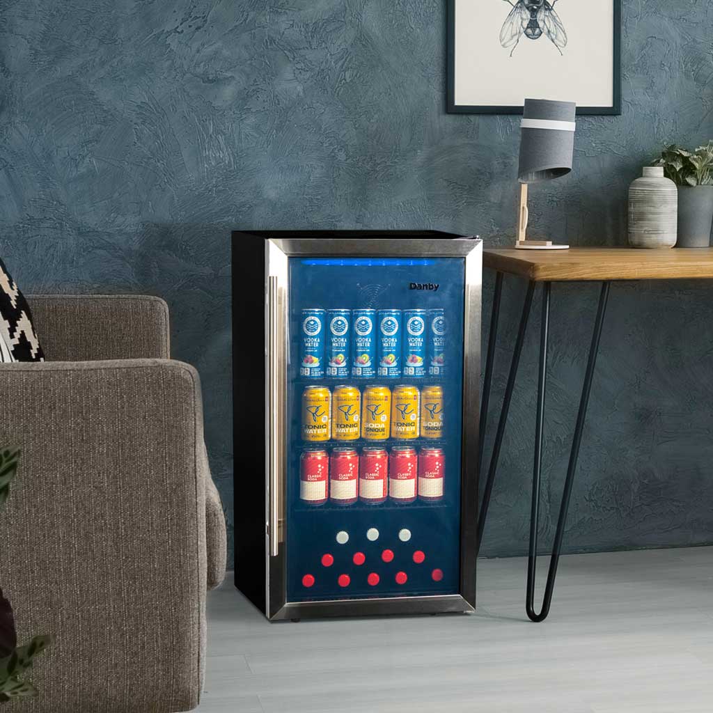 Danby 3.1 cu. ft. Free-Standing Beverage Center in Stainless Steel 5 Danby appliances 3.1 cu ft beverage center stainless DBC117A2BSSDD-6 shown in a living room beside a sofa and table with beverage cans visible through glass door