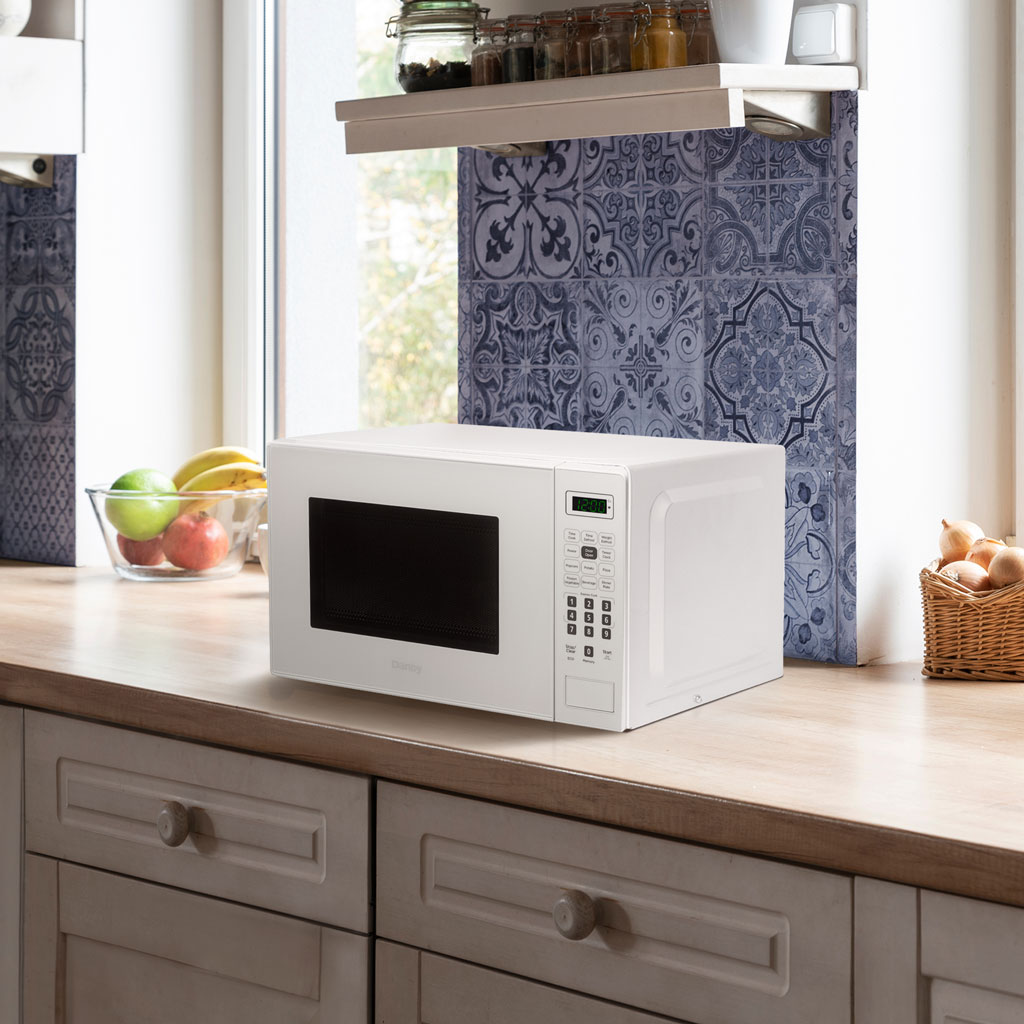 Micro-ondes 0,7 pi³ sur pied Danby blanc 5 Micro-ondes de comptoir Danby DBMW0721BWW de 0,7 pi³ sur un comptoir de cuisine à côté d'armoires et d'accessoires de cuisine