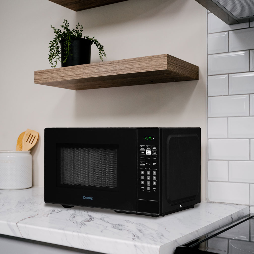 Micro-ondes de comptoir Danby DBMW0921BBB de 0,9 pi³ sur un comptoir à côté d'accessoires de cuisine et d'armoires