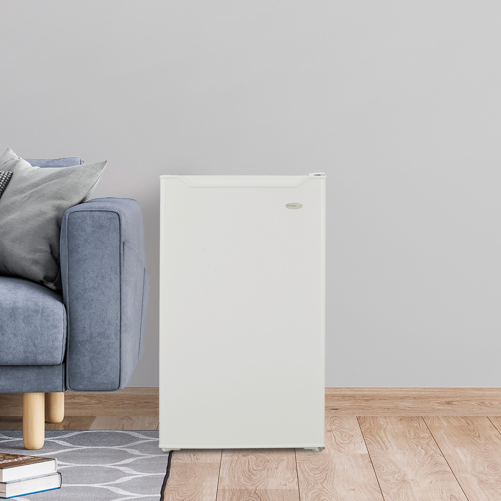 Danby appliances 4.4 cu ft compact fridge white DCR044B1WM shown beside a chair in a living room setting highlighting compact placement and everyday use
