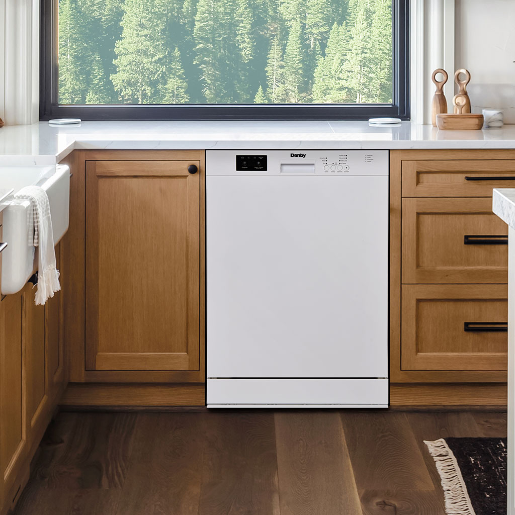 Danby appliances built in dishwasher 24 inch DDW2400EW installed in a modern kitchen with wood cabinetry, white countertop, and large window above, shown in a front view highlighting flush built-in design