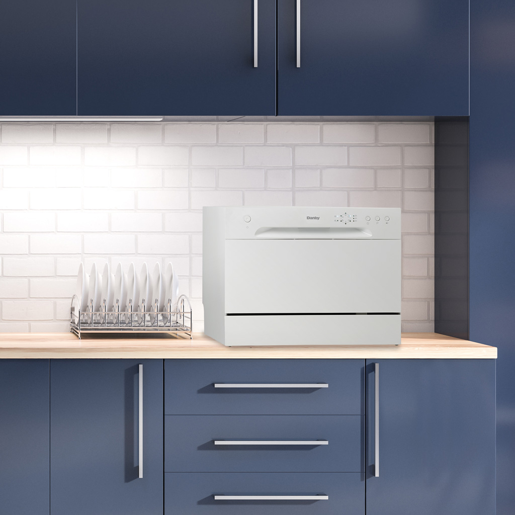 Danby 6 Place Setting Countertop Dishwasher in White 5 Danby appliances 6 place setting countertop dishwasher white DDW621WDB placed on a kitchen countertop with blue cabinetry and white tile backsplash shown in a front view
