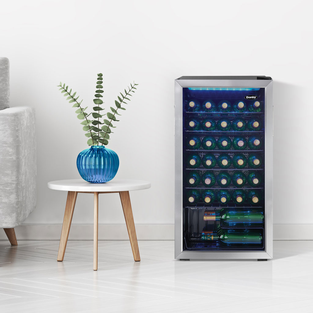 Danby 36 Bottle Free-Standing Wine Cooler in Stainless Steel 4 Danby appliances 36 bottle wine cooler stainless DWC036A1BSSDB-6 shown in a home setting beside a stool and plant with wine bottles visible through glass door