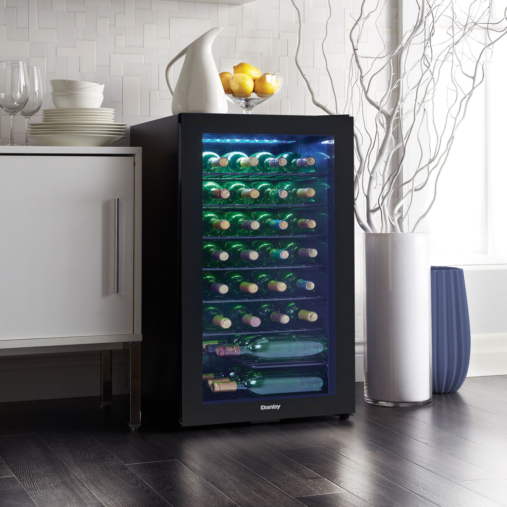 Danby 36 Bottle Free-Standing Wine Cooler in Black 4 Danby appliances 36 bottle wine cooler black DWC036A2BDB-6 shown in a kitchen setting beside cabinetry and flooring, displaying interior shelves with wine bottles visible through glass door