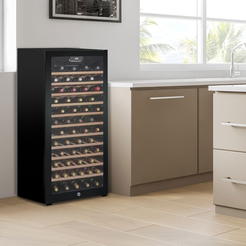 Danby 94 Bottle Free-Standing Wine Cooler in Black 5 Danby appliances 94 bottle wine cooler black DWC094L1B shown in a kitchen beside cabinetry and window with interior wooden shelves stocked with wine bottles visible through glass door