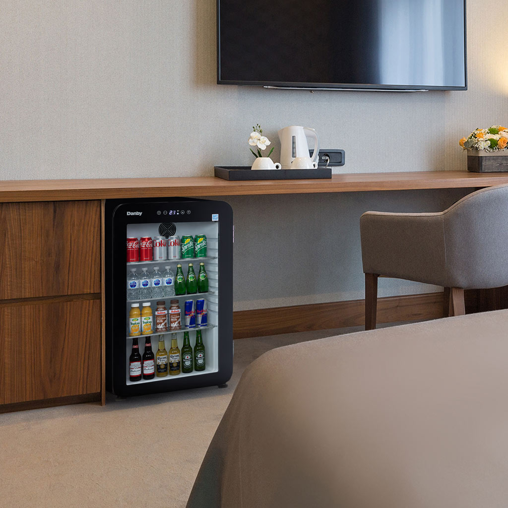 3.3 cu ft mini fridge Black glass door with soda cans, water bottles and beer on shelves in bedroom setting